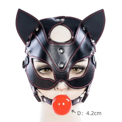 Máscara BDSM con ball gag rojo de 4.2 cm de diámetro, fabricada en cuero sintético negro con detalles metálicos. Diseño de gato para juegos sexuales.